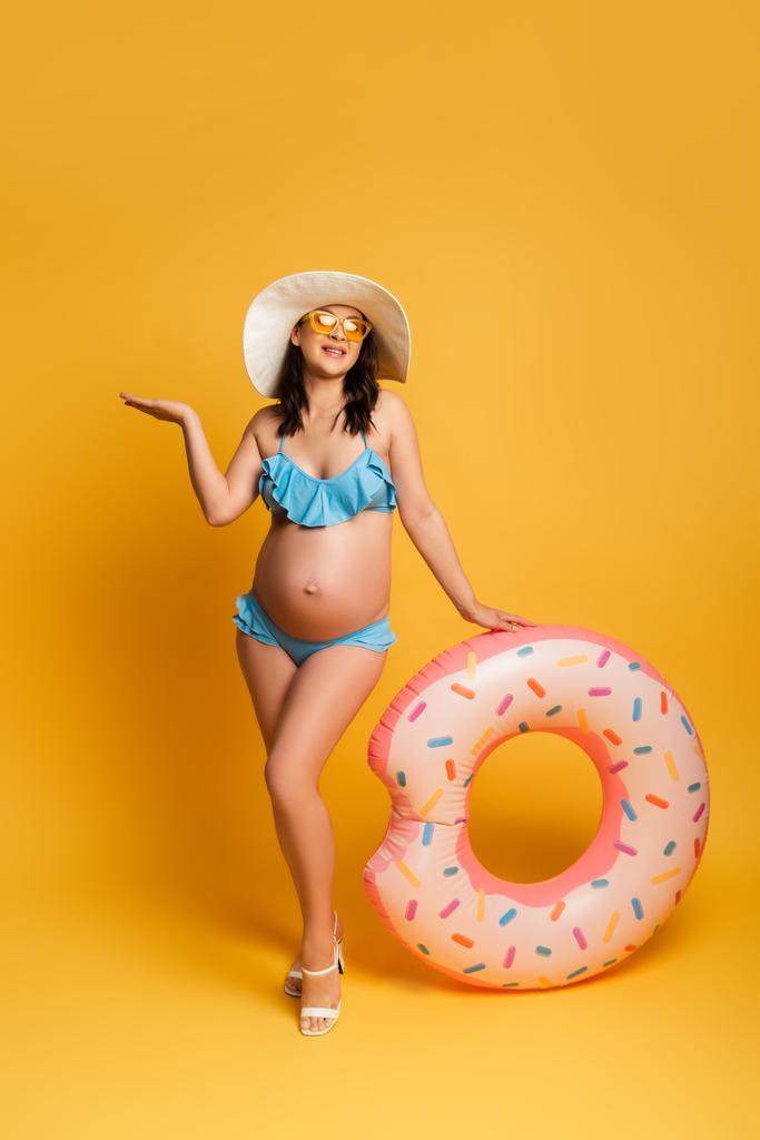 vue pleine longueur de la femme enceinte avec anneau de natation posant sur jaune - Photo, image
