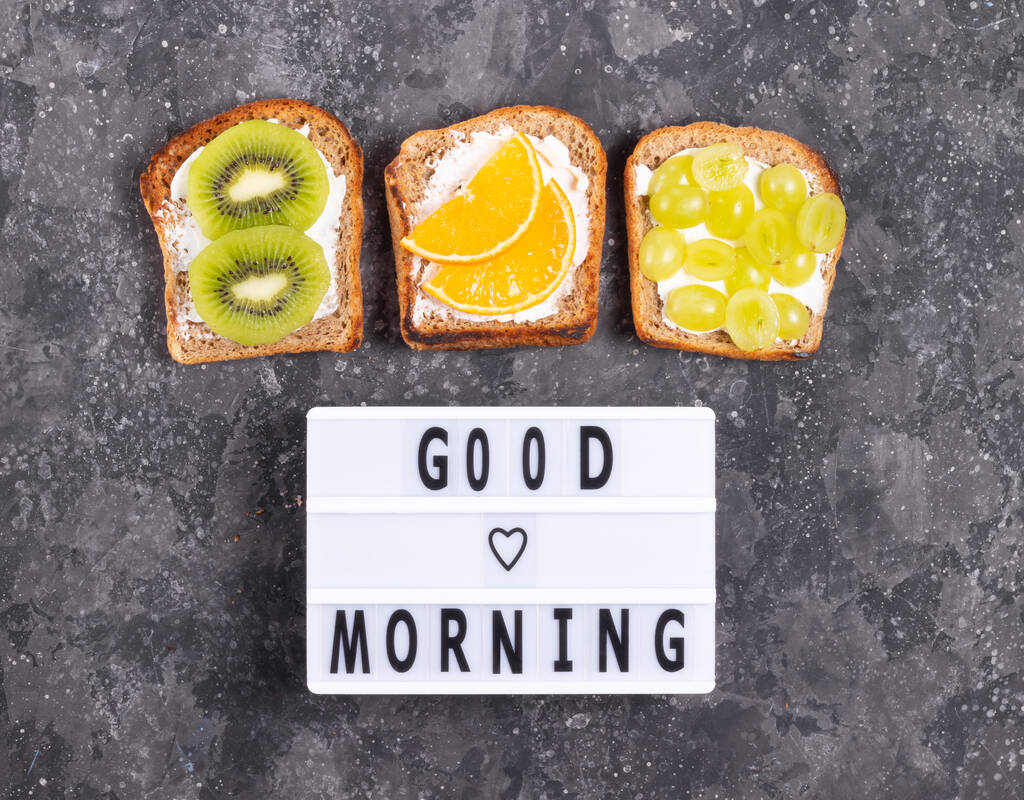 Надпись доброе утро с фруктовыми бутербродами со сливочным сыром на сером фоне - Фото, изображение