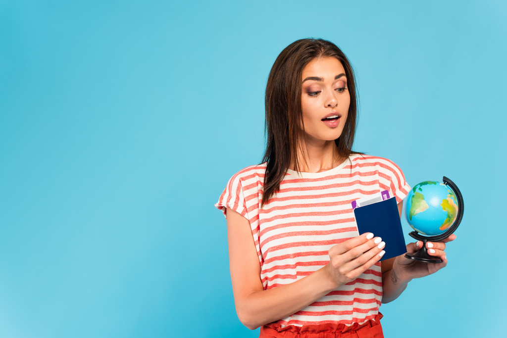 surprise fille tenant passeport et regardant globe isolé sur bleu - Photo, image