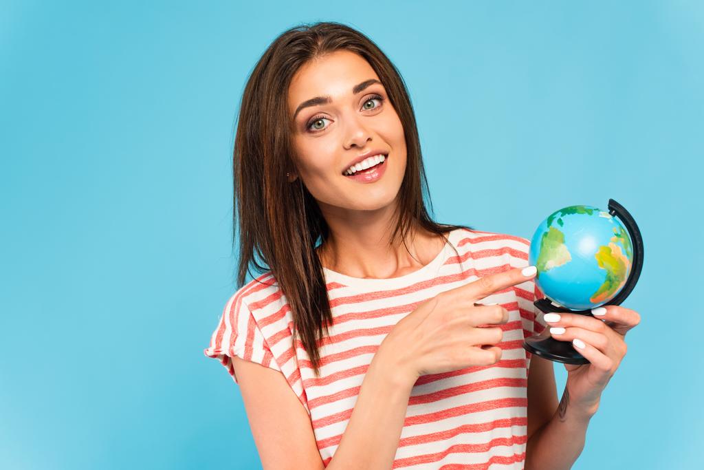 happy girl pointing with finger at globe isolated on blue - Photo, Image