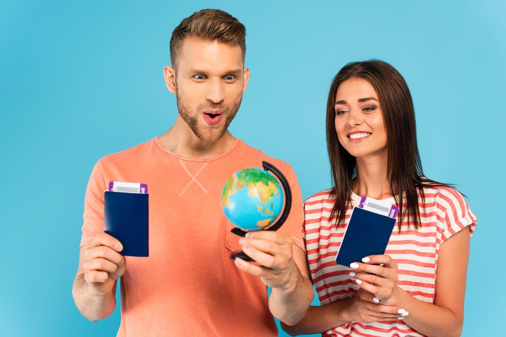 glückliches Paar blickt auf Globus, während es Pässe isoliert auf blauem Grund hält - Foto, Bild