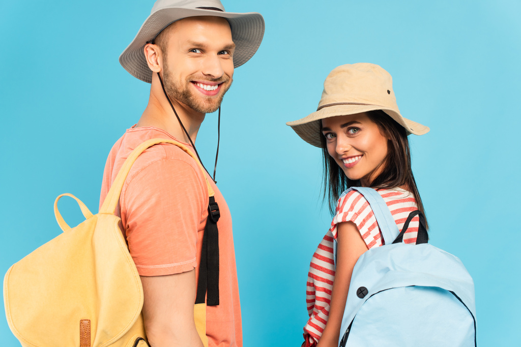 szczęśliwy podróżnicy w kapelusze patrząc na aparat odizolowany na niebiesko - Zdjęcie, obraz