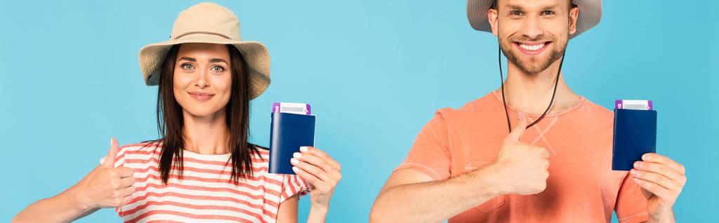 панорамний знімок щасливого чоловіка і жінки в капелюхах, що тримає паспорти і показує великі пальці вгору ізольовані на синьому
 - Фото, зображення