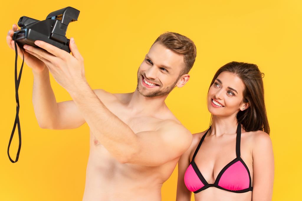 feliz homem sem camisa tomando selfie com namorada na câmera vintage isolado no amarelo
 - Foto, Imagem