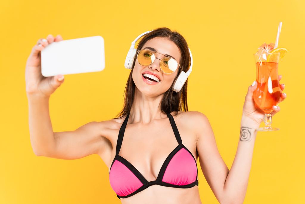menina alegre e tatuado em óculos de sol tomando selfie enquanto segurando coquetel isolado no amarelo
  - Foto, Imagem