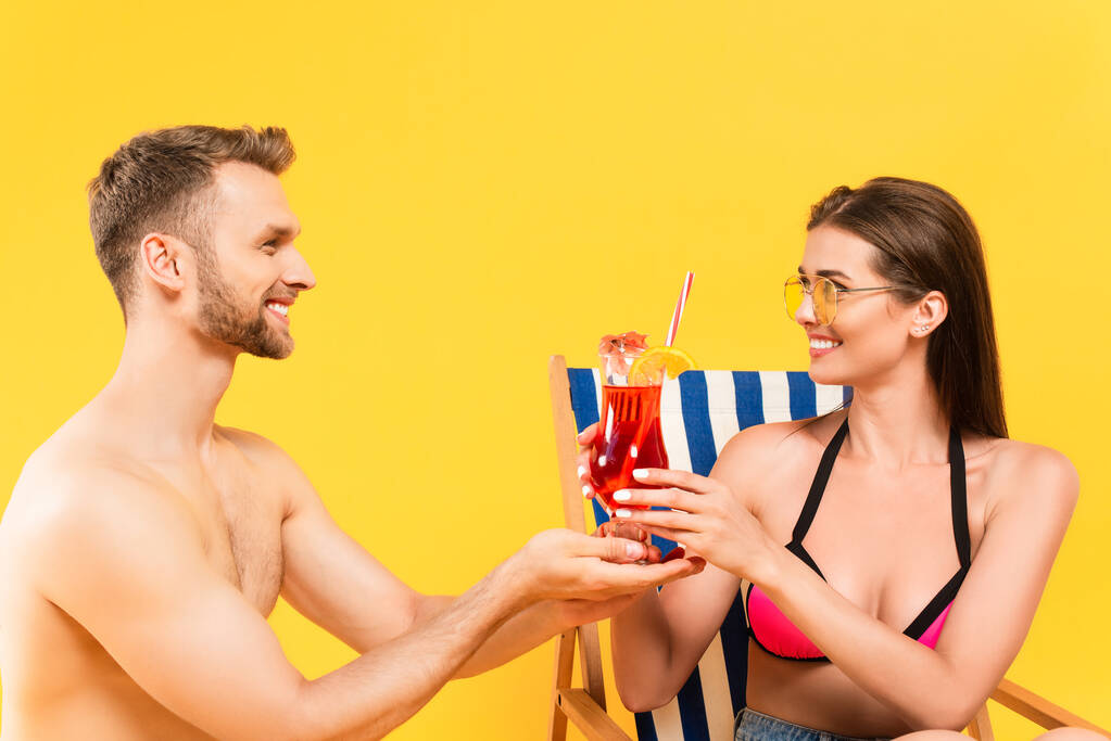 bärtiger Mann mit Cocktail in der Nähe attraktiver und glücklicher Mädchen in Sonnenbrille isoliert auf gelb - Foto, Bild