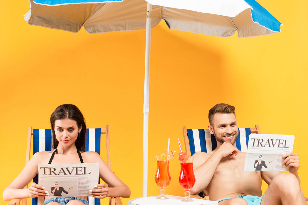 幸せなカップルは旅行新聞を読んで黄色のデッキチェアに座って - 写真・画像