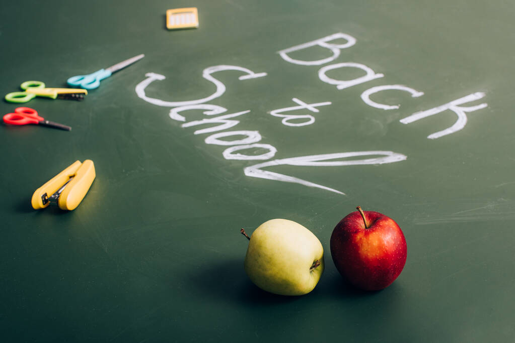 selective focus of delicious apples near back to school inscription and school supplies on green chalkboard - Photo, Image