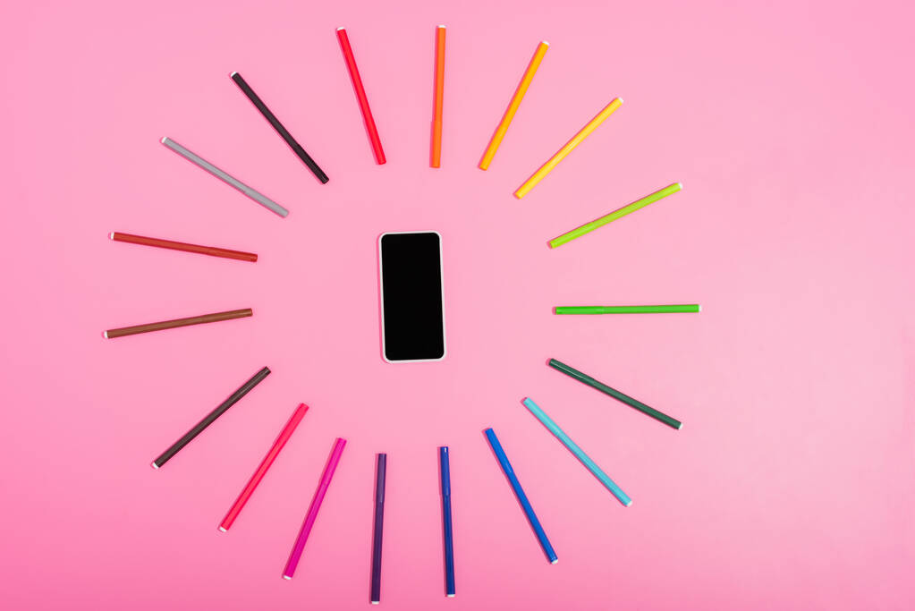 vista superior del smartphone con pantalla en blanco enmarcado por rotuladores multicolores en rosa
 - Foto, imagen
