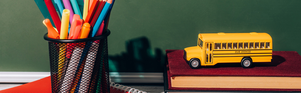 immagine orizzontale del modello di scuolabus sui libri vicino al portapenne con cancelleria sul taccuino vicino alla lavagna verde - Foto, immagini