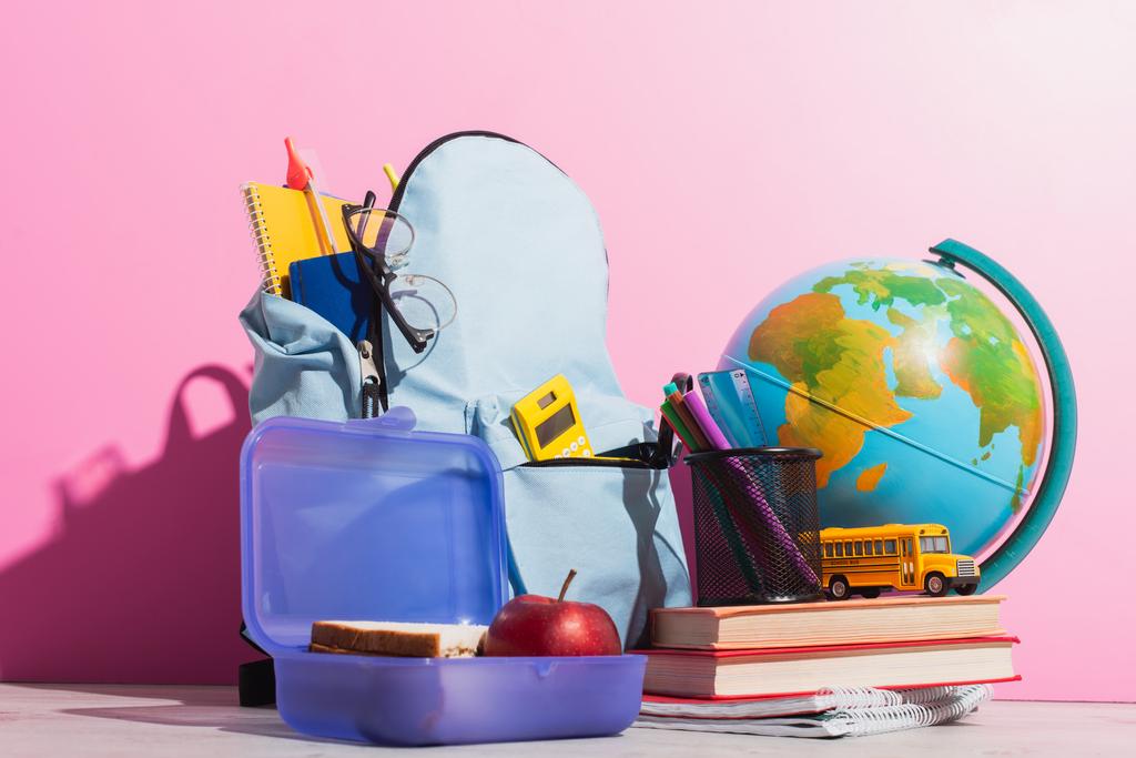 給食ボックスや世界中の文房具やスクールバスの模型やピンクの本でいっぱいのスクールバックパック - 写真・画像