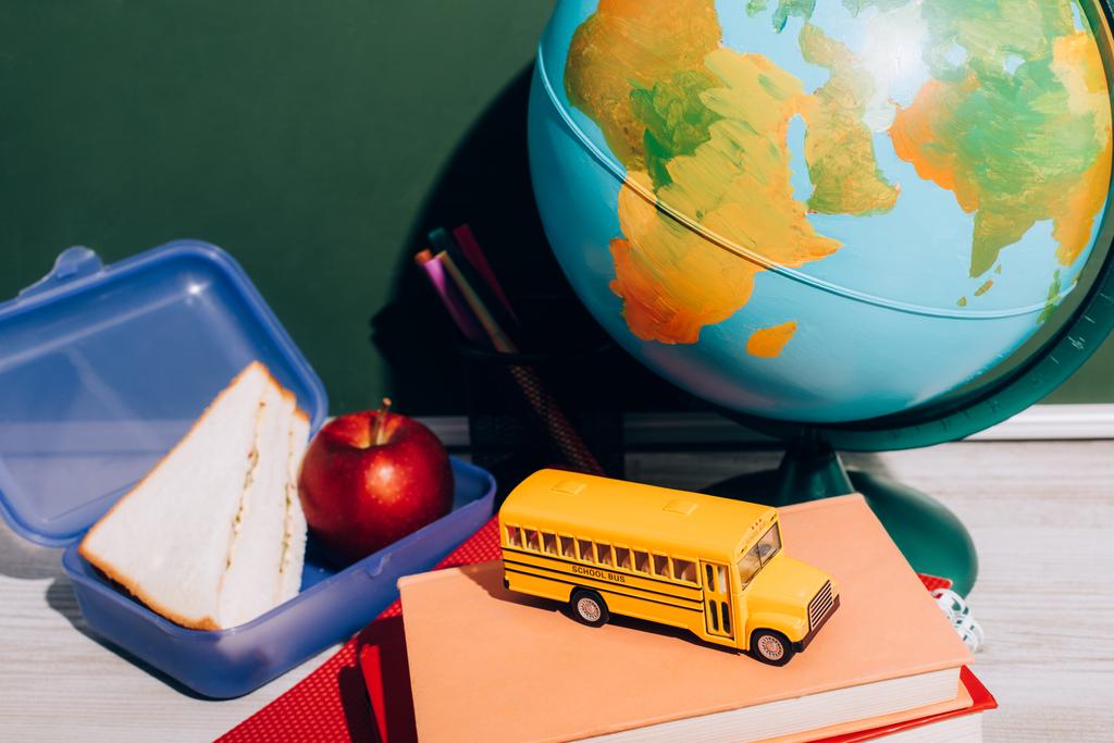 zeměkoule u oběda box a školní autobus model na knihách v blízkosti zelené tabuli - Fotografie, Obrázek