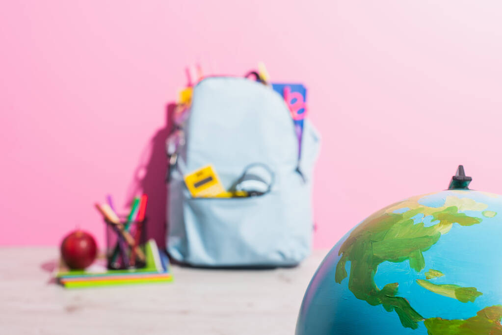 селективный фокус земного шара рядом рюкзак упакован со школьной канцелярской принадлежностью, держателем ручки и спелых яблок - Фото, изображение