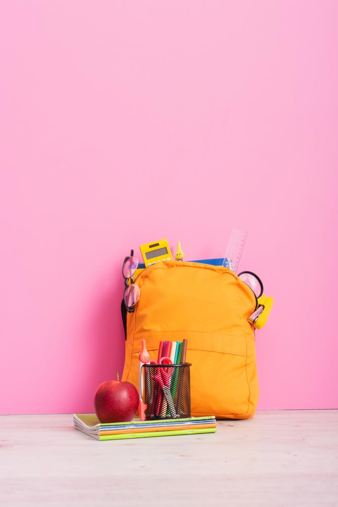 συσκευασμένα σακίδιο σχολείο κοντά notebook, κάτοχος στυλό με γραφική ύλη και ώριμο μήλο σε ροζ - Φωτογραφία, εικόνα