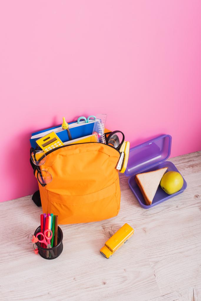 высокий угол зрения рюкзак со школьными принадлежностями рядом с моделью школьного автобуса, коробка для обеда и держатель ручки с войлочными ручками и ножницами на розовом - Фото, изображение
