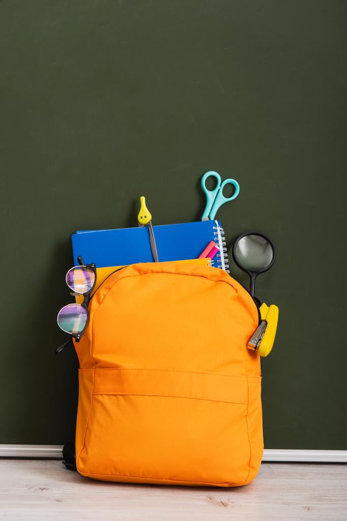žlutý batoh se školními potřebami na stole v blízkosti zelené tabule - Fotografie, Obrázek