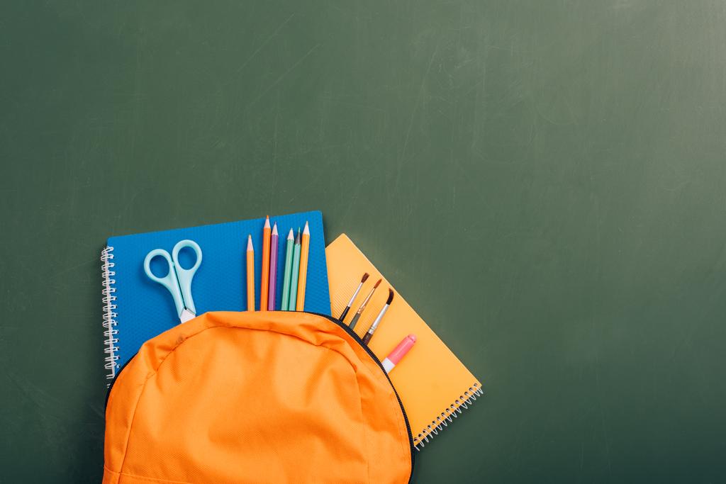 mochila escolar com livros de cópia coloridos, lápis de cor, tesoura e pincéis em quadro-negro verde
 - Foto, Imagem