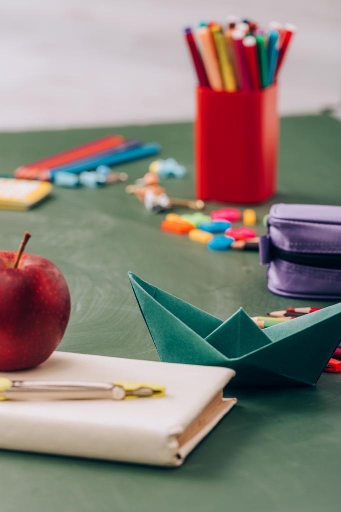 Selektiver Fokus von reifem Apfel und Kompassteiler auf Buch in der Nähe von Schulschreibwaren auf grüner Kreidetafel  - Foto, Bild
