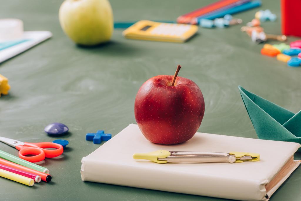 selective focus of ripe apple on book near school stationery on green chalkboard - Photo, Image