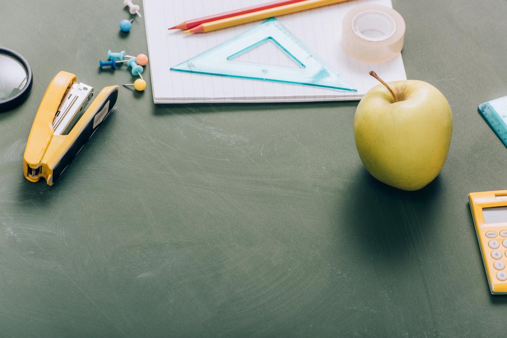 спелое яблоко, копировальная книга и школьные принадлежности на зеленой доске - Фото, изображение