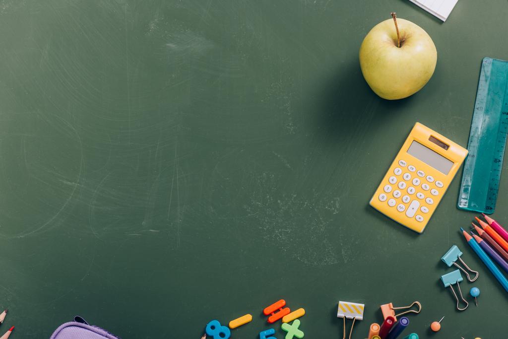 верхний вид спелых яблоко и калькулятор возле школьных принадлежностей на зеленой доске - Фото, изображение