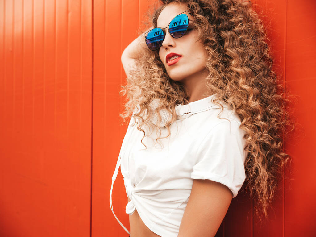 Kaunis hymyilevä malli afro kiharat kampauksen pukeutunut kesällä hipster clothes.Sexy huoleton tyttö poseeraa lähellä punainen seinä outdoors.Funny ja positiivinen nainen hauskaa aurinkolasit - Valokuva, kuva