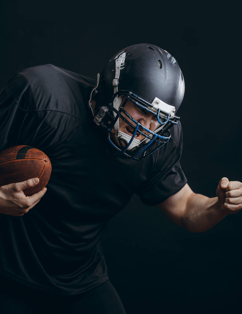 Football américain sportif joueur en action isolé sur le mur noir studio - Photo, image