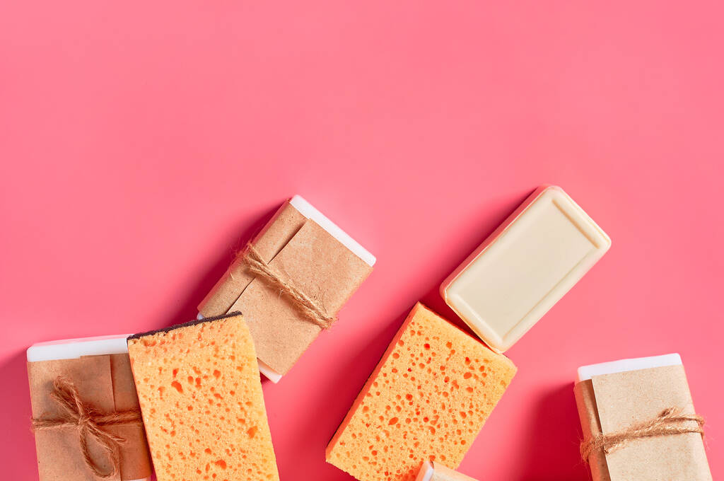 Heap of bricks of soap in vintage packing and sponges on pink background. Hygiene and cleaning concept - Photo, Image