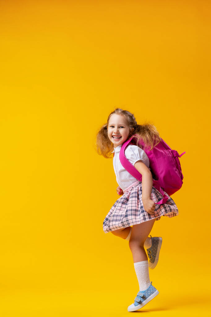χαρούμενη άτακτη μαθήτρια με στολή με σακίδιο πηδάει σε κίτρινο φόντο Δυναμικές εικόνες που επιστρέφουν στην ιδέα του σχολείου. έναρξη των διακοπών. Πίσω στο σχολείο. Το αγόρι είναι έτοιμο να μελετήσει.. - Φωτογραφία, εικόνα