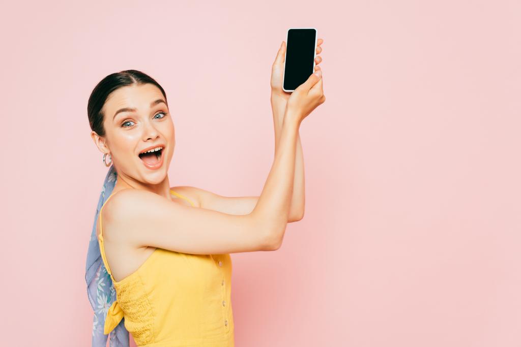 Вид сбоку молодой брюнетки, держащей смартфон в изоляции на розовом фоне - Фото, изображение