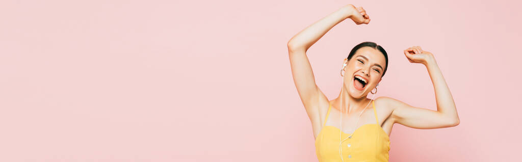 vzrušená brunetka mladá žena ve sluchátkách tanec izolované na růžové, panoramatický záběr - Fotografie, Obrázek