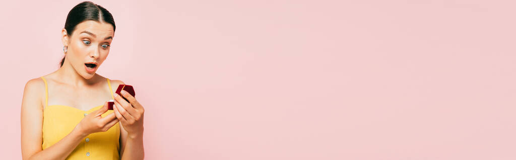 järkyttynyt brunette nuori nainen tilalla laatikko kihlasormus eristetty vaaleanpunainen, panoraama laukaus - Valokuva, kuva