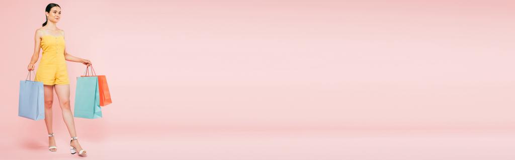 Вид брюнетки в полный рост с сумками на розовом фоне, панорамный снимок - Фото, изображение