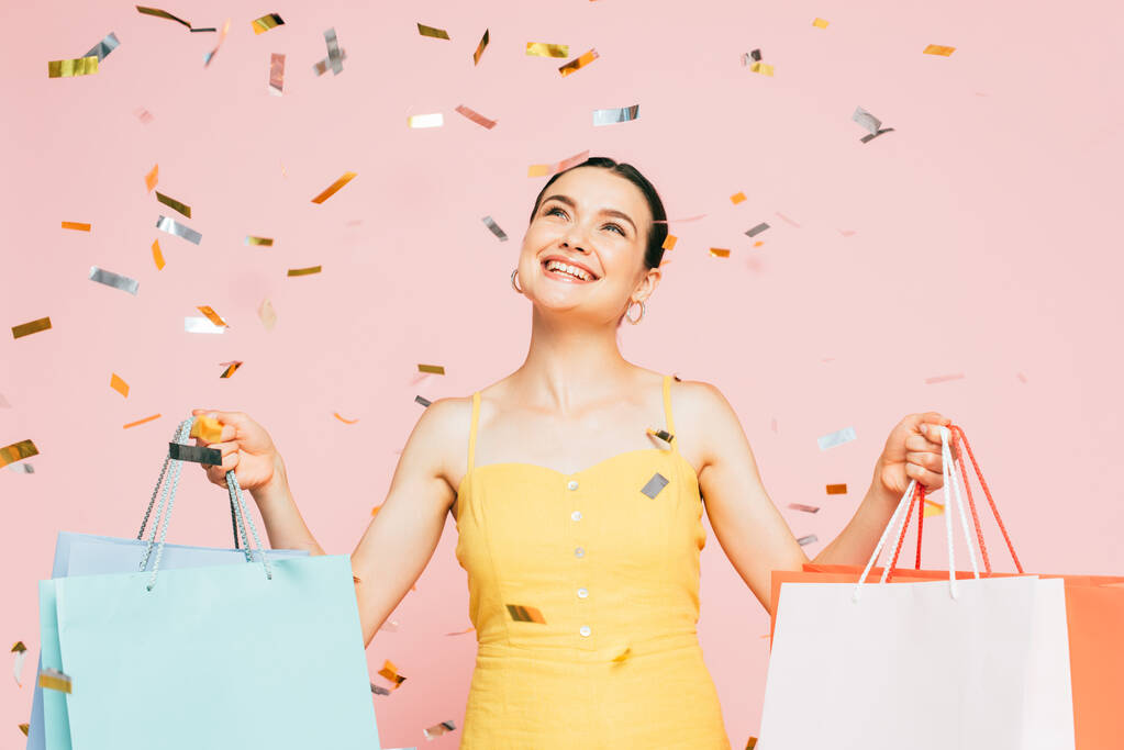 brunette nuori nainen ostoskassit alla kuuluvat confetti eristetty vaaleanpunainen - Valokuva, kuva
