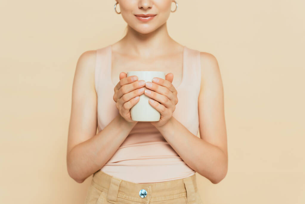 bijgesneden weergave van jonge vrouw met witte mok geïsoleerd op beige - Foto, afbeelding
