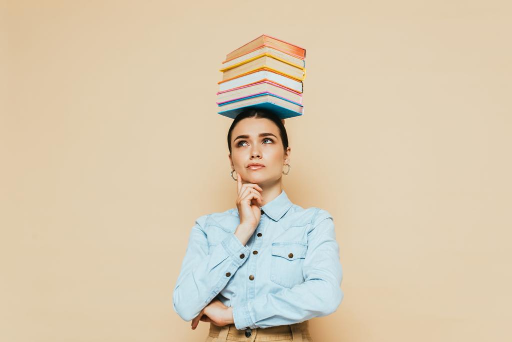 estudante pensativo em camisa jeans com livros na cabeça isolado em bege
 - Foto, Imagem