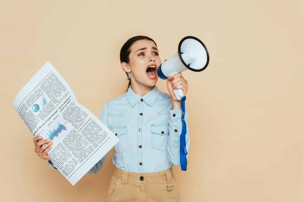 μελαχρινή γυναίκα σε denim πουκάμισο με εφημερίδα ουρλιάζοντας σε ηχείο απομονωμένο σε μπεζ - Φωτογραφία, εικόνα