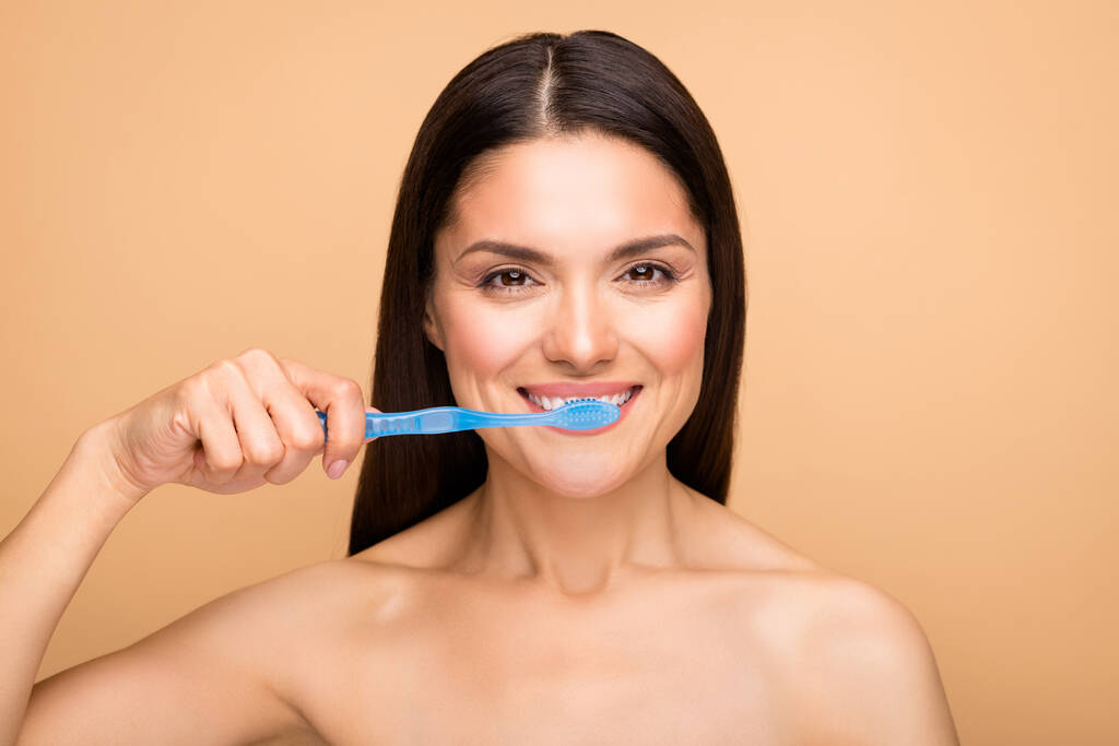 Κοντινό πλάνο φωτογραφία του ελκυστική λατινική γυμνή κυρία κρατώντας μπλε οδοντόβουρτσα καθαρισμού λευκά δόντια χρήση νέων menthol πάστα απομονωμένη μπεζ παστέλ χρώμα φόντο - Φωτογραφία, εικόνα