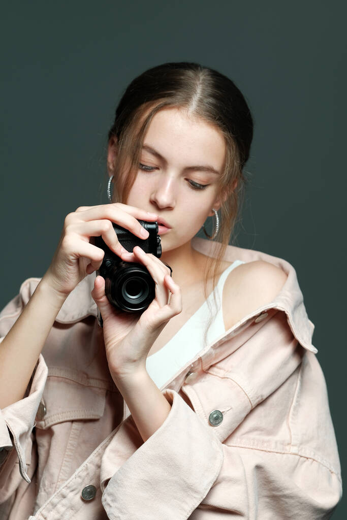 Dívka fotografka v růžové bundě drží v rukou bezzrcadlovou kameru. - Fotografie, Obrázek