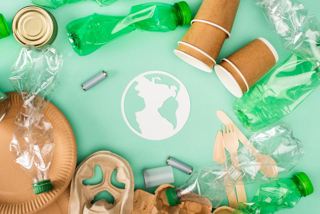 Vue du dessus des bouteilles en plastique, accumulateurs et vaisselle jetables près du panneau de terre de papier sur fond vert, concept d'écologie - Photo, image