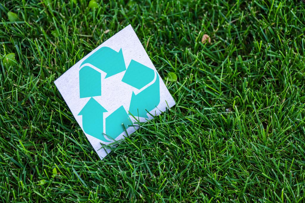Vista de alto ângulo do cartão com símbolo de reciclagem na grama verde ao ar livre, conceito de ecologia
 - Foto, Imagem