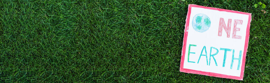 Πανοραμική φωτογραφία του πλακάτ με μία γη γράμματα στο πράσινο γρασίδι σε εξωτερικούς χώρους, έννοια οικολογία - Φωτογραφία, εικόνα
