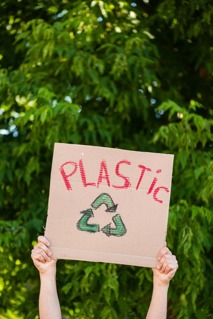 Vista recortada del hombre sosteniendo pancarta con letras de plástico y reciclar letrero con árboles en el fondo, concepto de ecología  - Foto, Imagen