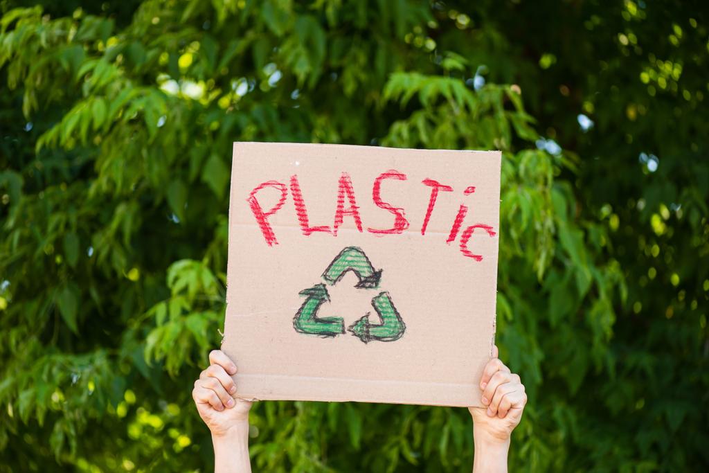 Vista parziale dell'uomo che tiene cartello con segno di plastica riciclare con alberi sullo sfondo, concetto di ecologia - Foto, immagini