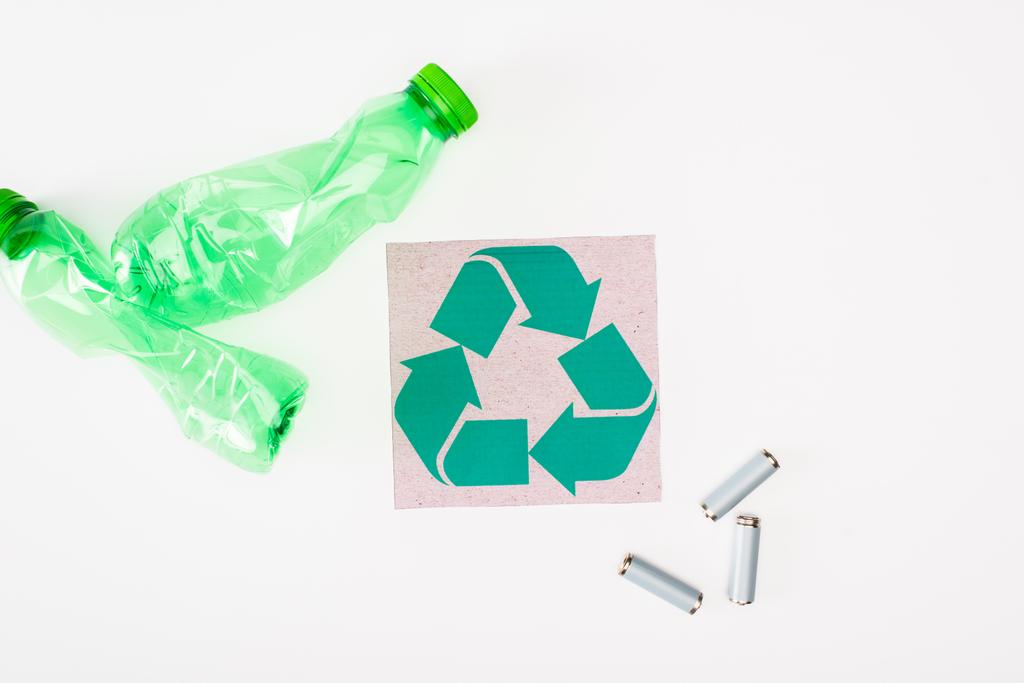 Vue du dessus de la carte avec panneau de recyclage près des bouteilles et accumulateurs en plastique froissés sur fond blanc, concept d'écologie - Photo, image