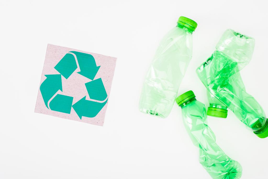 Top view of card with recycle sign near crumpled plastic bottles on white background, ecology concept - Photo, Image