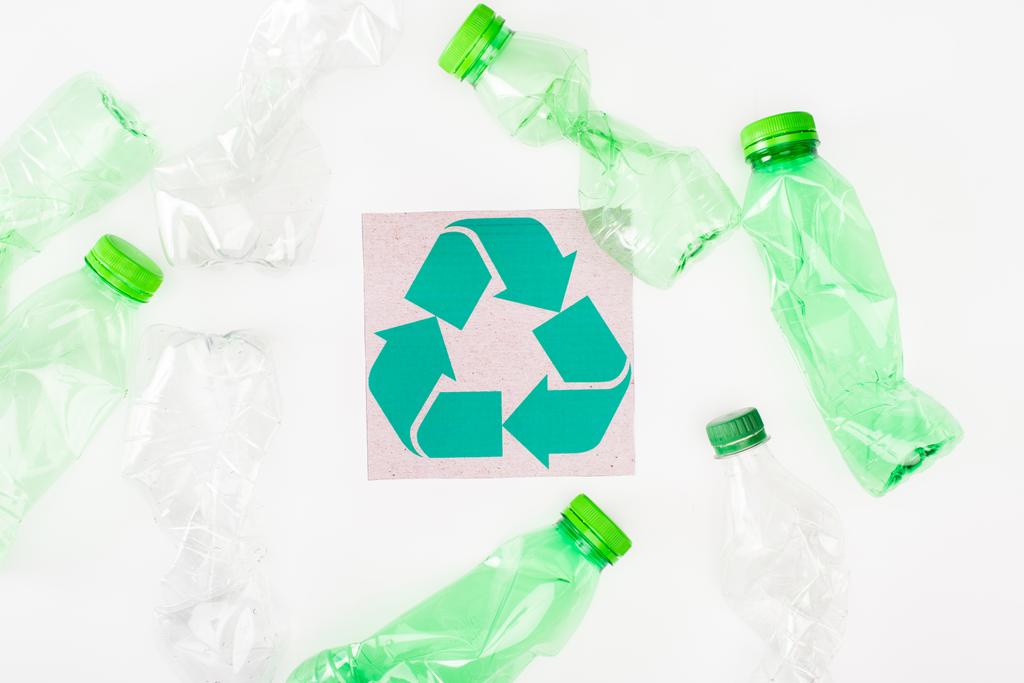 Top view of crumpled plastic bottles near card with recycle sign on white background, ecology concept - Photo, Image