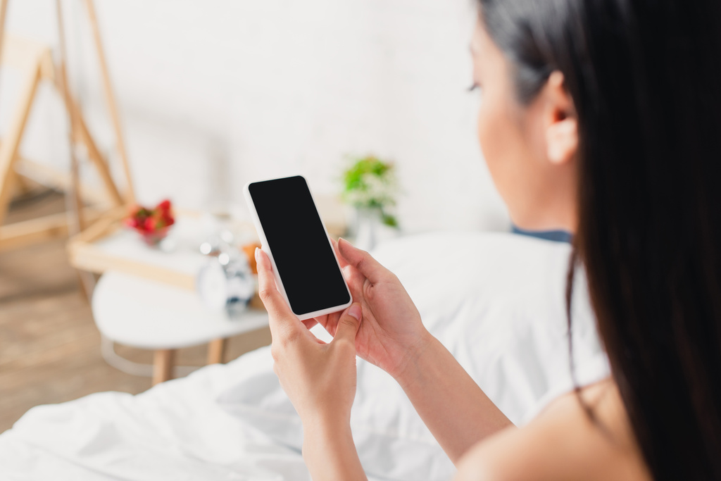 foyer sélectif de la jeune femme asiatique tenant smartphone avec écran vide sur le lit  - Photo, image