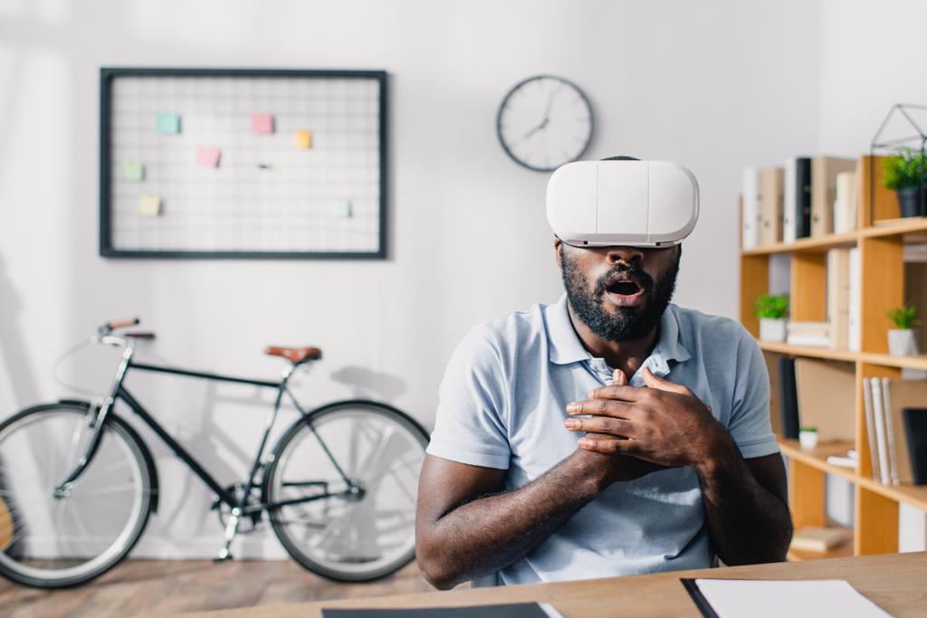 Enfoque selectivo de empresario afroamericano emocionado usando auriculares de realidad virtual en la mesa en la oficina  - Foto, imagen