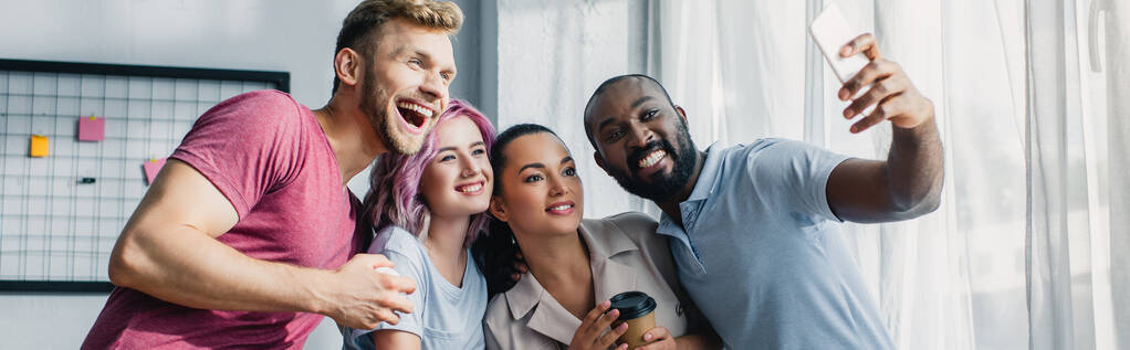 Imagem horizontal de pessoas multiétnicas de negócios tirando selfie com smartphone no escritório
  - Foto, Imagem